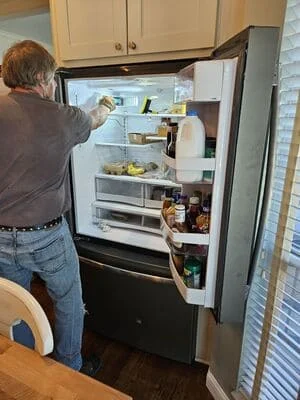 Technician inspecting interior components of French-door refrigerator with shelves and cooling system visible