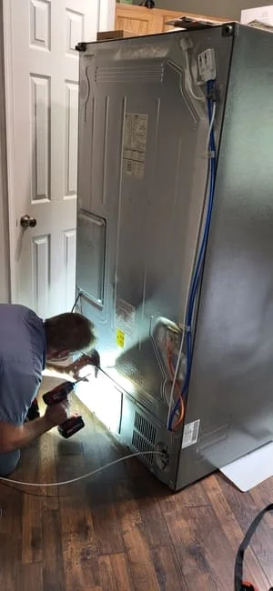 Technician servicing interior components of stainless steel refrigerator with diagnostic tools