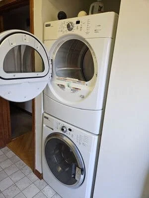 White stacked front-load washer and dryer with open dryer door in laundry room