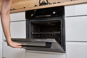 Technician servicing black built-in wall oven with open door and visible interior racks