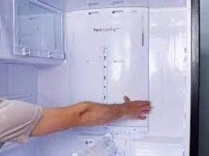 Technician inspecting refrigerator interior shelving and cooling system components
