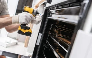 Technician repairing oven interior components with tools and white gloves