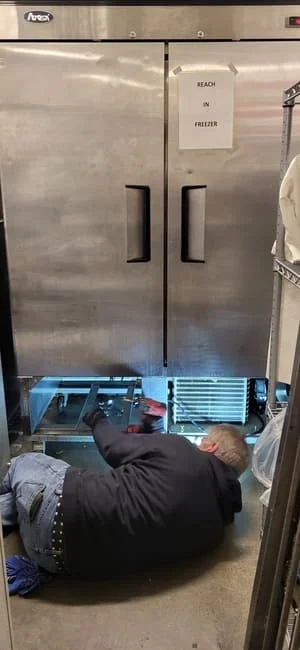 Technician servicing stainless steel commercial reach-in freezer with dual doors and diagnostic equipment