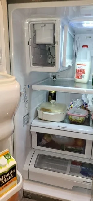 Open refrigerator showing disassembled ice maker housing and internal dispenser components