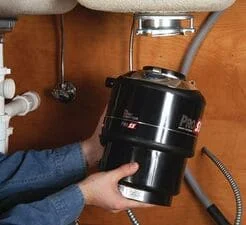 New black garbage disposal unit installed under sink with plumbing connections