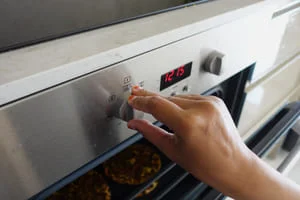 Technician adjusting stainless steel oven control panel with digital display