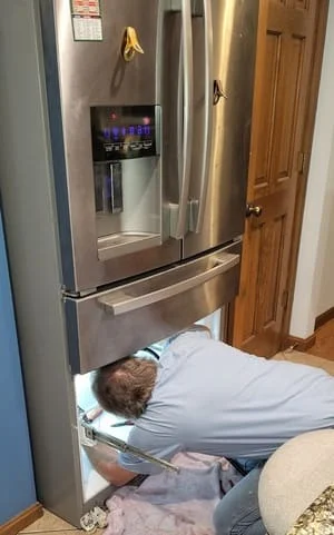 Technician servicing stainless steel French door refrigerator with ice dispenser
