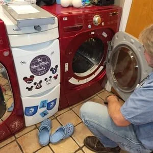 A Cincinnati appliance repair technician inspecting the interior drum and heating element of a residential dryer during a home service call. The dryer panel is open and diagnostic tools are visible on the laundry room floor.