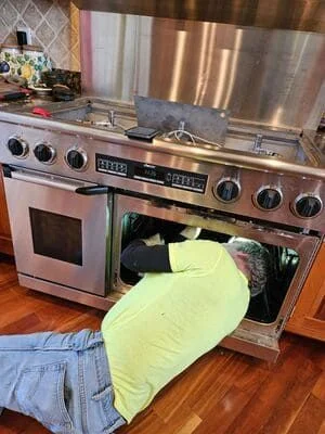 A Reliable Refrigeration and Appliance Repair technician inspecting the interior heating element of a residential electric oven in a Cincinnati home kitchen. The oven door is open and the technician is using a diagnostic tool to test the element.